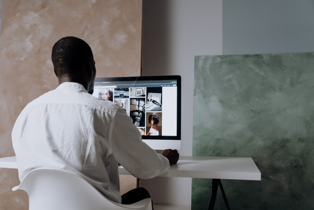 Services Back view of a man sitting at a computer, browsing images in a modern workspace.